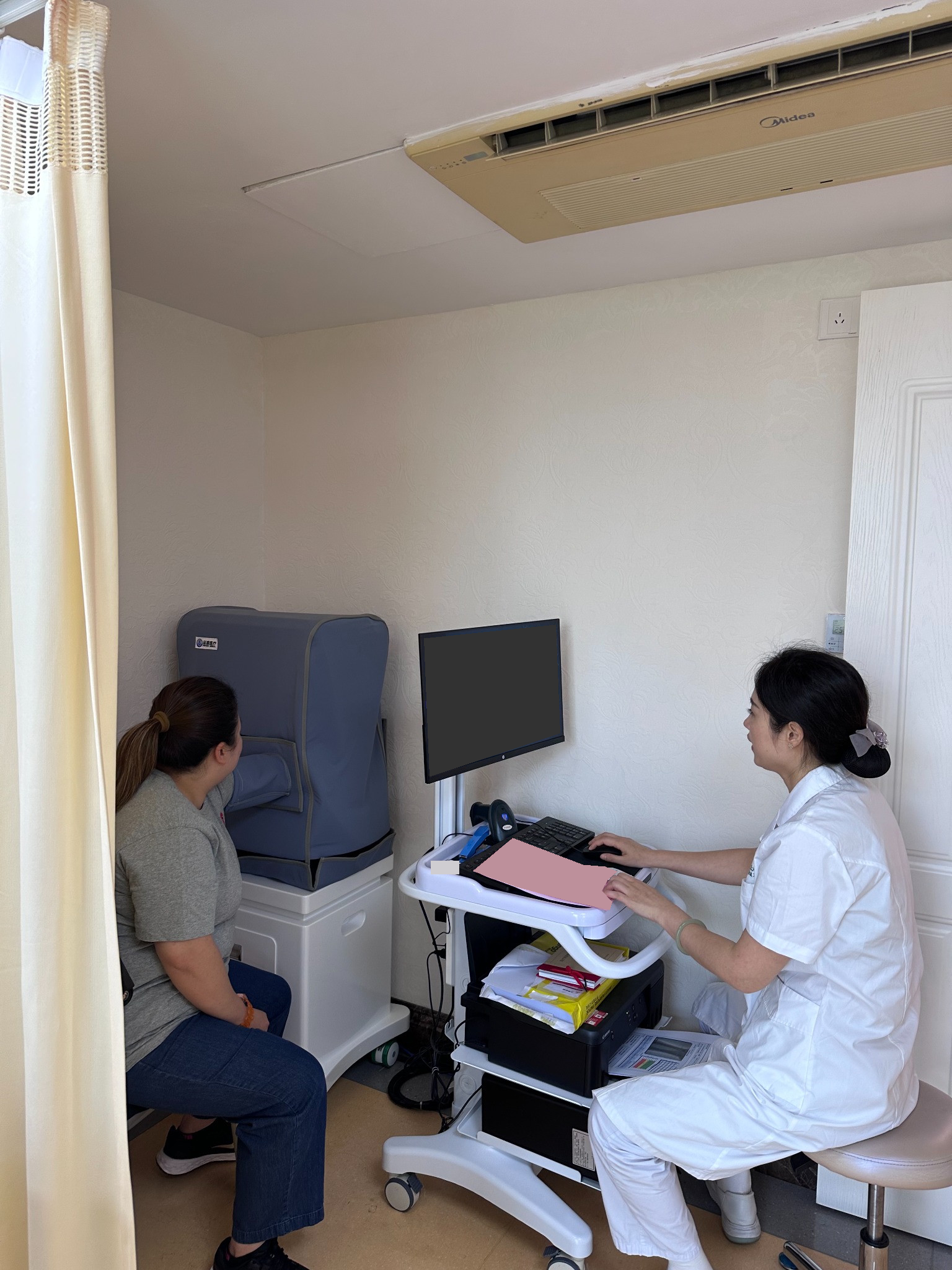 A visitor and hospital clinician during an examination, with the screen and paperwork obscured