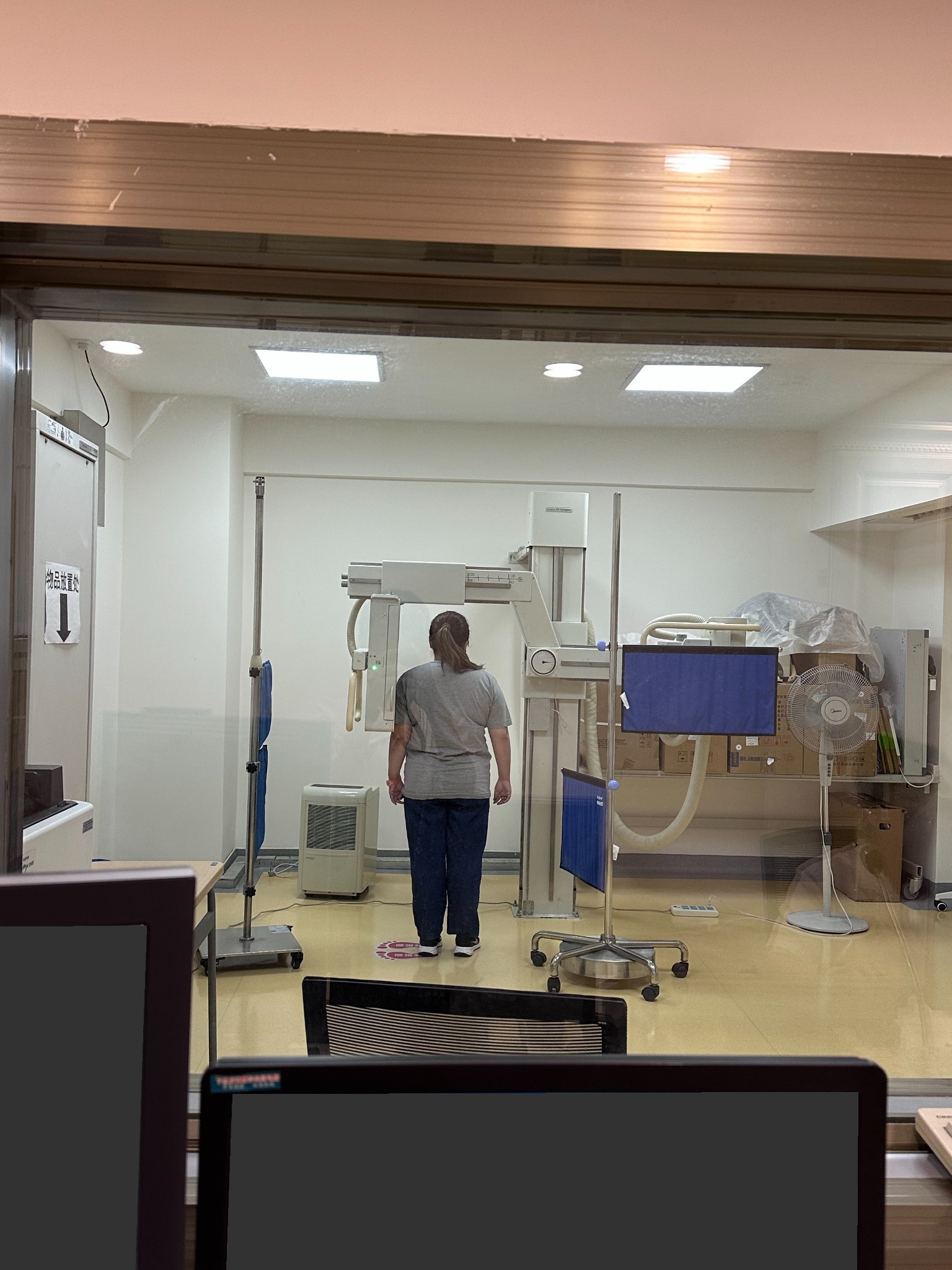 A visitor positioned for a standing radiography examination, with foreground screens obscured